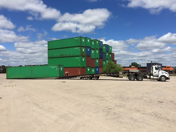 a delivery truck flatbed next to a stack of green and red shipping containers