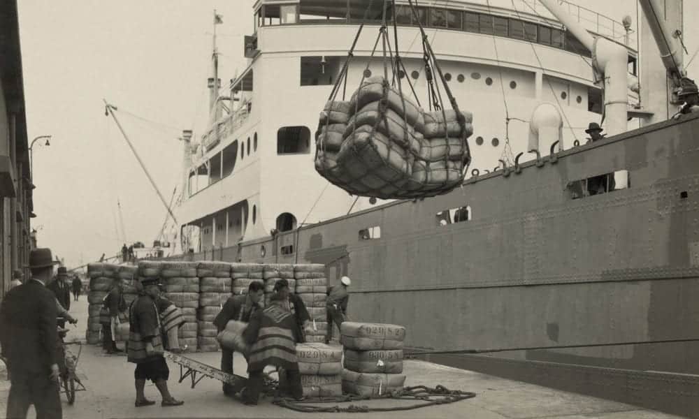 black and white photo of old ship being unloaded by crane